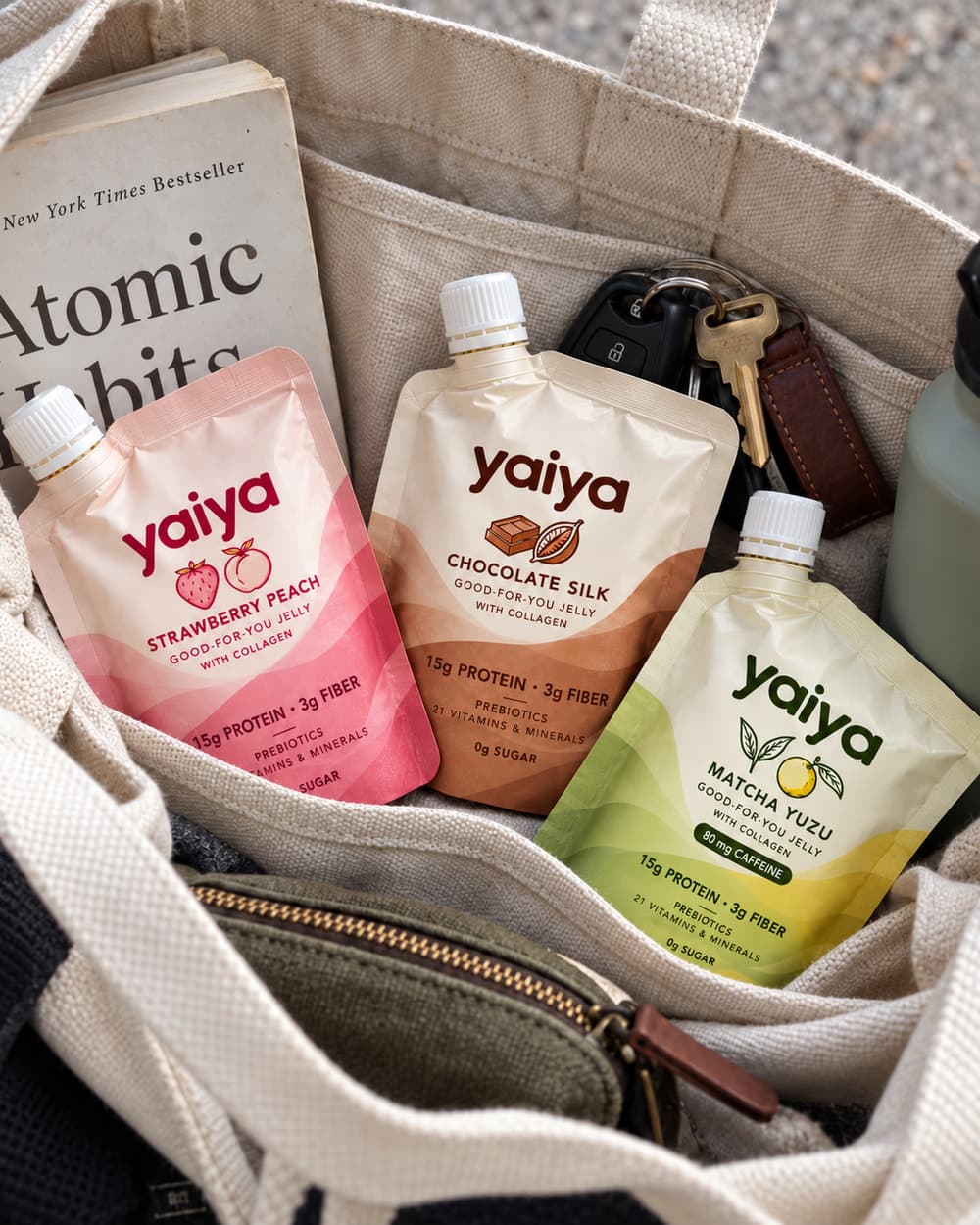 Strawberry Peach, Chocolate Silk and Matcha Yuzu pouches in an open canvas tote with a book, car keys and a water bottle.